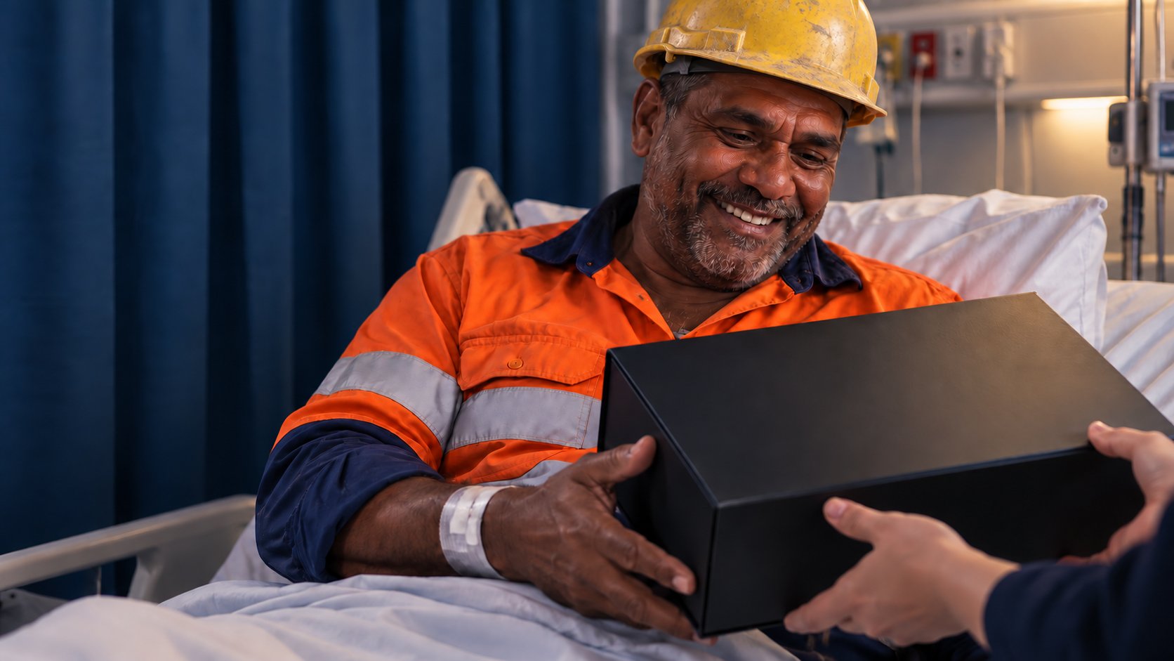 Tradie in a hard hat and hi-vis smiling as he receives a Hard Hat Hampers gift box